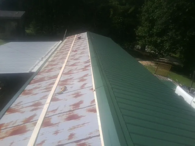Old rusted panels beside newly installed green metal roofing — Wind Damage Roof Repair by Roofing Brothers in Cameron